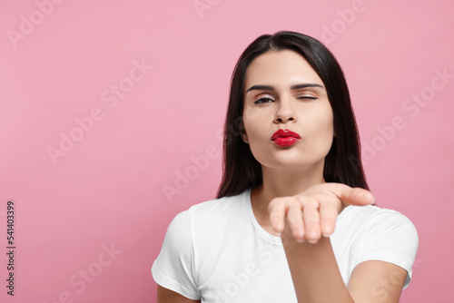 Beautiful young woman blowing kiss on pink background. Space for text