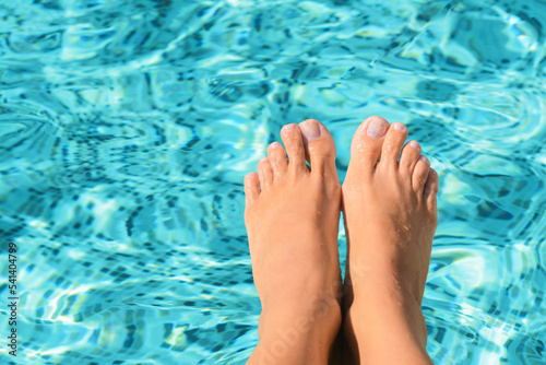 Woman holding feet on surface of water in pool, closeup