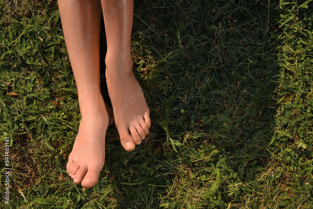 Woman sitting barefoot on green grass outdoors, top view. Space for text