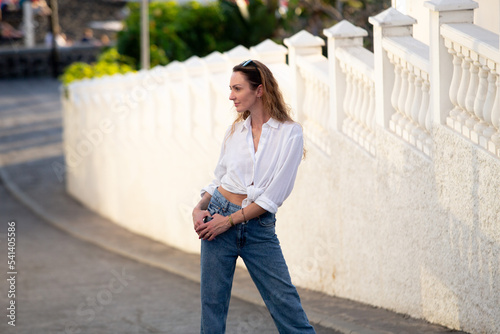 Modern attractive stylish young woman in trendy t-shirt with blue jeans posing on the street. Cute European girl enjoying a summer day outside.