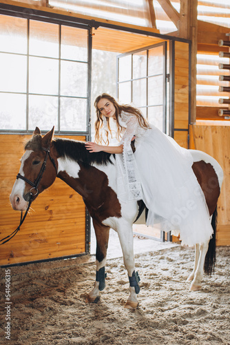 A charming boho bride rides a horse on a ranch at sunset in winter. © dsheremeta