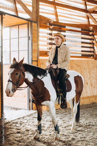 Handsome cowboy man riding a horse on a ranch.