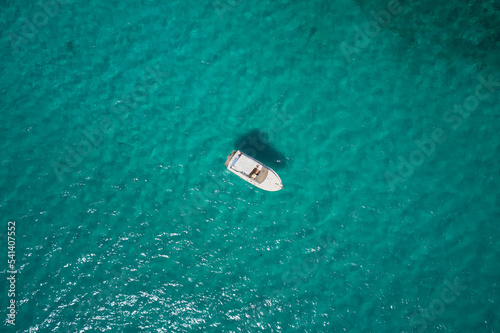 White boat at anchor, transparent turquoise water aerial view. White boat blue water top.