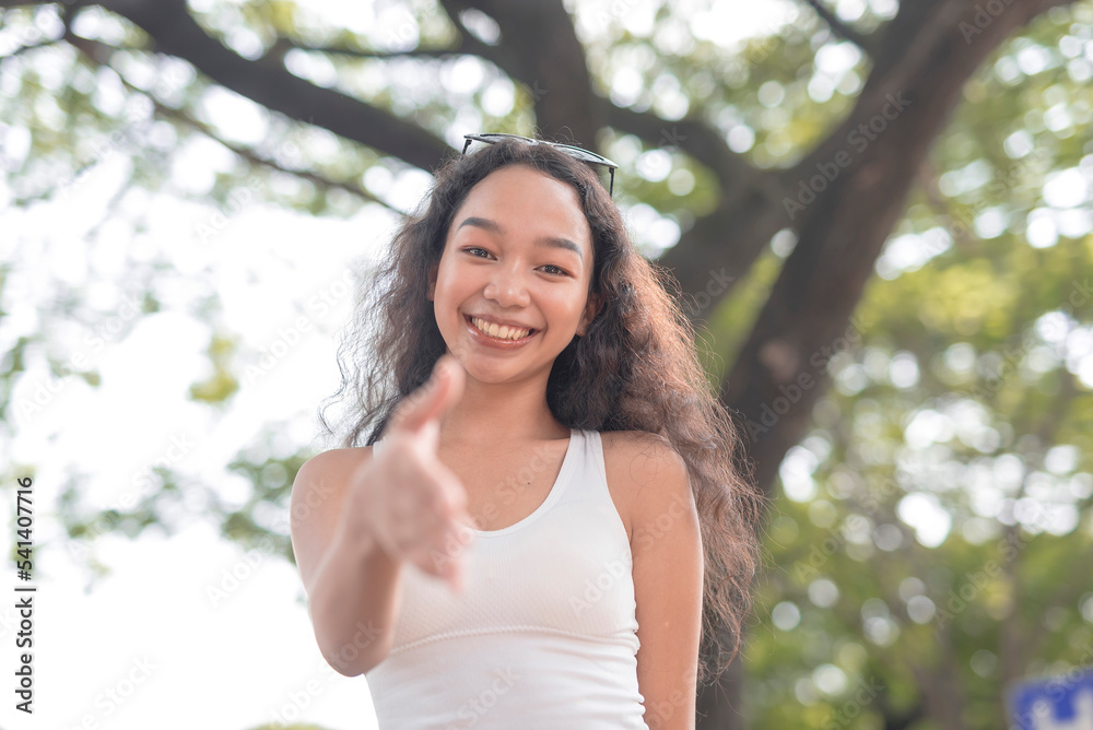 A low-angle photo of a smiling Asian lady extending her hand as she initiates a handshake. A low-angle photo of a smiling Asian lady extending her hand as she initiates a handshake.
