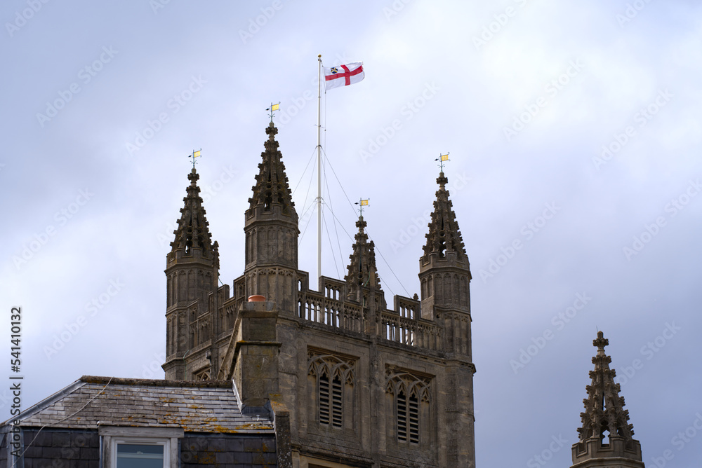 Tower with flag of famous Abbey Church of Saint Peter and Saint Paul at City of Bath on a blue cloudy summer day. Photo taken August 2nd, 2022, Bath, United Kingdom. Tower with flag of famous Abbey Church of Saint Peter and Saint Paul at City of Bath on a blue cloudy summer day. Photo taken August 2nd, 2022, Bath, United Kingdom.