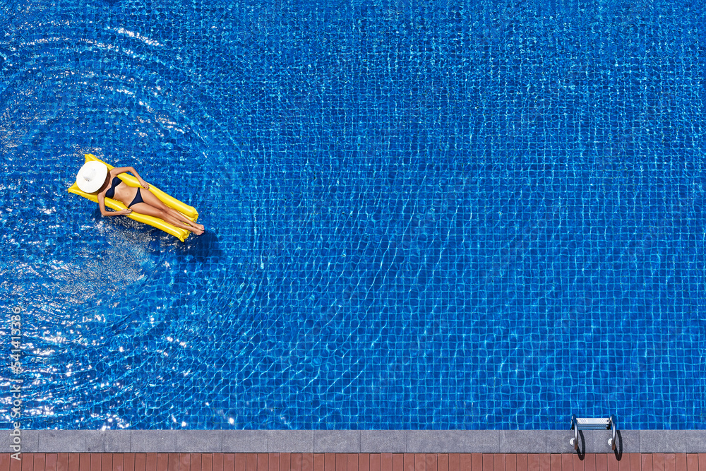 Enjoying suntan. Vacation concept. Top view of slim young woman in bikini on the yellow air mattress in the big swimming pool.