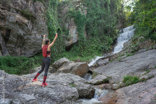 Young fitness woman running at forest trail on waterfall background