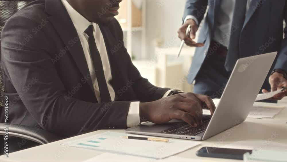 Cropped of African American businessman in elegant black suit working on laptop in modern office Cropped of African American businessman in elegant black suit working on laptop in modern office