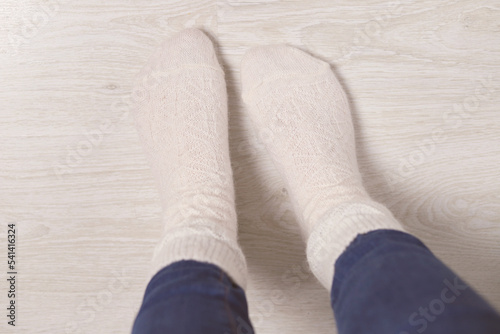 Women's feet in knitted, woolen white socks at home on a light floor. Cold floor in the apartment.Top view