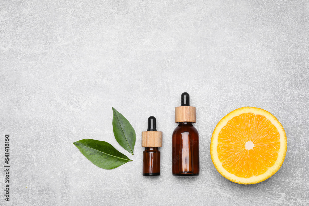 Bottles of essential oil with orange slice and leaves on grey table, flat lay Bottles of essential oil with orange slice and leaves on grey table, flat lay