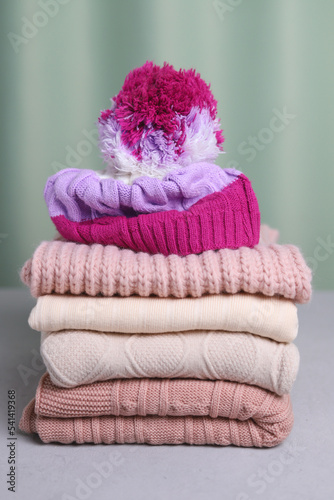 A bright knitted hat is lying on a stack of sweaters. Vertical photo. Warming clothes.