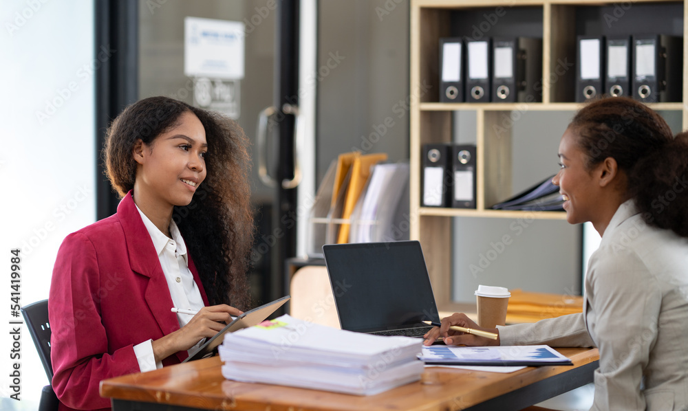 Two young African businesswomen are sitting and talking. Consulting business information showing results and agreeing to invest with a happy smile. Two young African businesswomen are sitting and talking. Consulting business information showing results and agreeing to invest with a happy smile.
