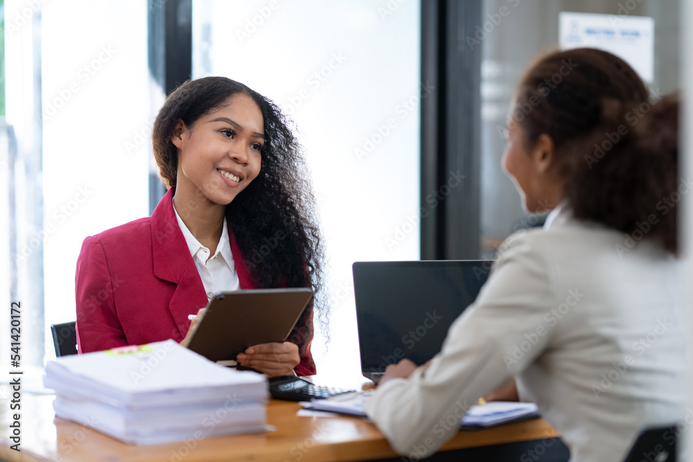 Two young African businesswomen are sitting and talking. Consulting business information showing results and agreeing to invest with a happy smile. Two young African businesswomen are sitting and talking. Consulting business information showing results and agreeing to invest with a happy smile.