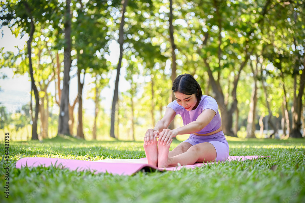 Fit young Asian woman stretching her legs and arms on yoga mat, practicing yoga