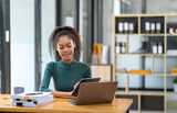 Smiling African American businesswoman sitting on a laptop thinking happily analyzing data