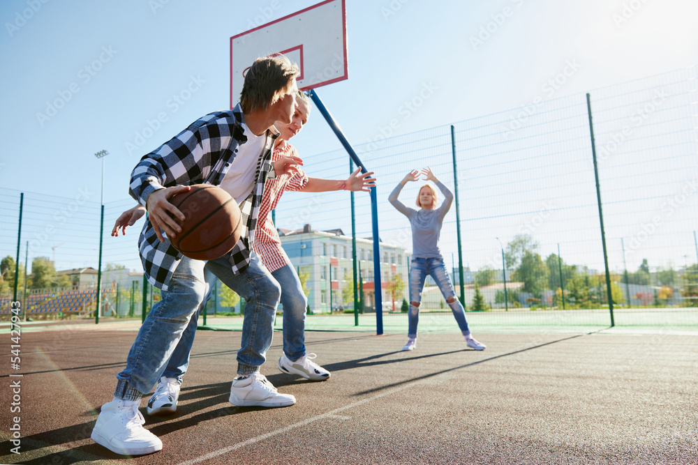 Obraz premium Group of teens, students playing street basketball at basketball court outdoors. Sport, leisure activities, hobbies, team, friendship