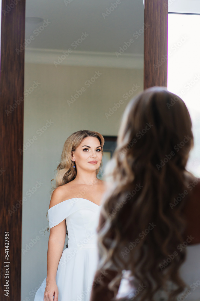Fototapeta premium beautiful blonde bride in a white dress looks at the reflection in the mirror. 