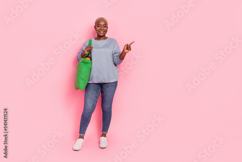 Full body photo of cheerful pretty person indicate finger empty space isolated on pink color background