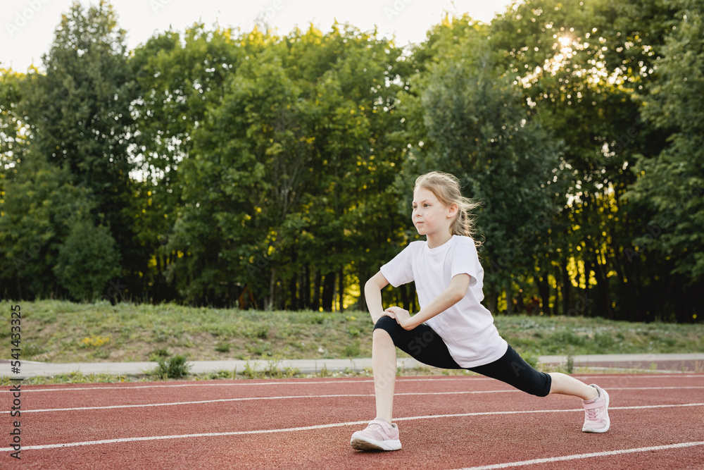Child girl warming up on the sports track before running