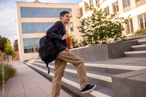 Fotografie Joyful teenager with a book and schoolbag ascending the steps