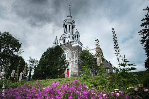 Low-angle shot of Saint Sauveur church in Canada surrounded by flowers and trees photo