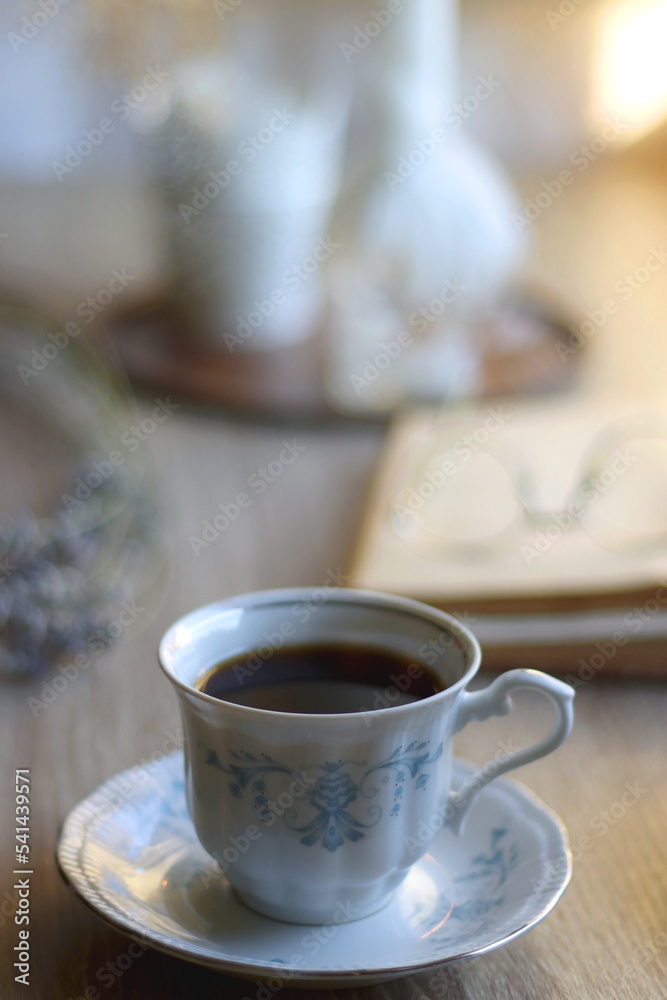 Cup of tea, plate with chocolate chip cookies, open book, reading glasses, lit candles and dry lavender flowers. Hygge at home, selective focus. Cup of tea, plate with chocolate chip cookies, open book, reading glasses, lit candles and dry lavender flowers. Hygge at home, selective focus.