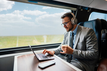 Handsome middle age businessman using his laptop computer while traveling with high-speed train. Modern and fast travel concept.