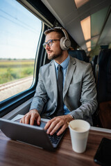 Handsome middle age businessman using his laptop computer while traveling with high-speed train. Modern and fast travel concept.