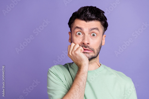 Photo of scared frightened guy with brunet hairstyle stubble wear t-shirt hold hand on chin staring isolated on purple color background