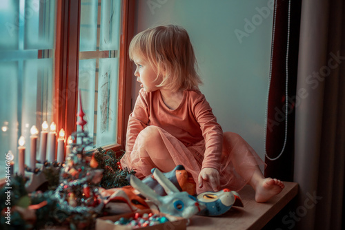 Cute little girl is dressing up a tiny Christmas tree and trying on New Year's animal masks. Image with selective focus and toning. 
