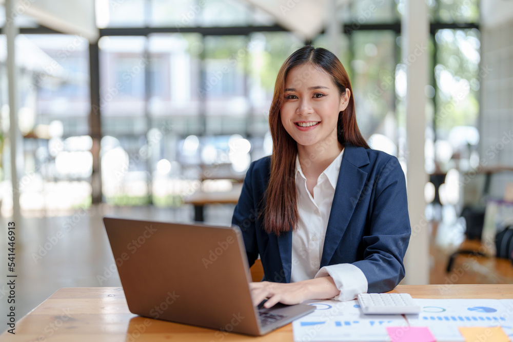 Portrait of smiling Asian businesswoman enjoying her hard work using her laptop at the office and looking at the camera. Portrait of smiling Asian businesswoman enjoying her hard work using her laptop at the office and looking at the camera.