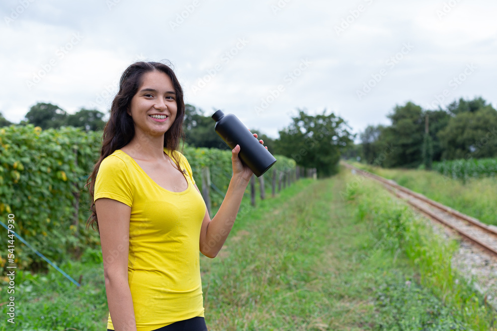 Young ethnic female athlete drinking water after training in nature 