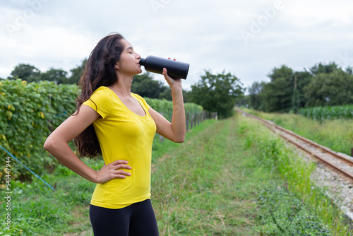 Young ethnic female athlete drinking water after training in nature 