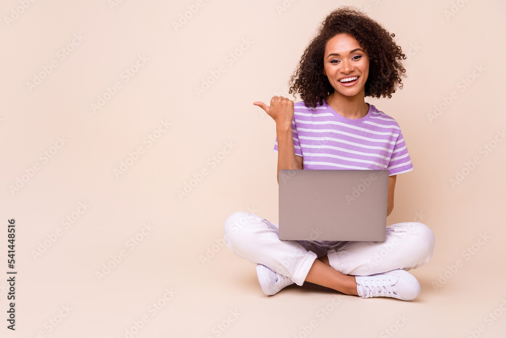 Photo of positive lovely nice girl brunette hair striped t-shirt indicating empty space hold netbook isolated on beige color background Photo of positive lovely nice girl brunette hair striped t-shirt indicating empty space hold netbook isolated on beige color background