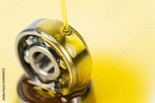 Closed up macro, Pouring automotive engine oil into ball bearing isolated on yellow oil background with copy space, engineering and industrial concept. Motor oil on bearing