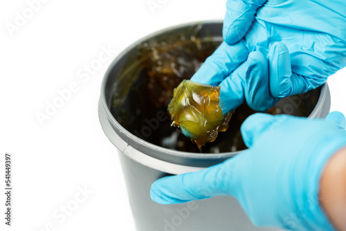 Worker use finger with glove to scoop up lithium grease from white plastic can in the laboratory. Yellow transparance grease on the finger. Testing and manufacturing concept