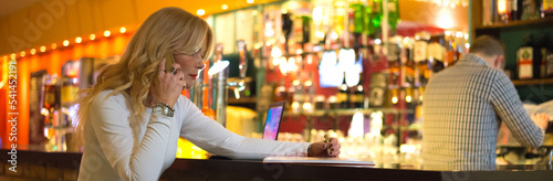 Elegant businesswoman working in the bar at night using laptop and smart phone