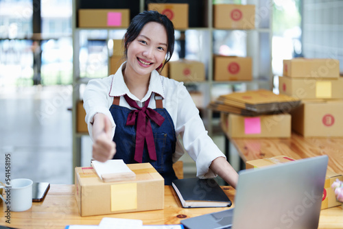 Starting small business entrepreneur of independent Asian woman smiling using computer laptop with cheerful success of online marketing package box items and SME delivery concept © Jirapong