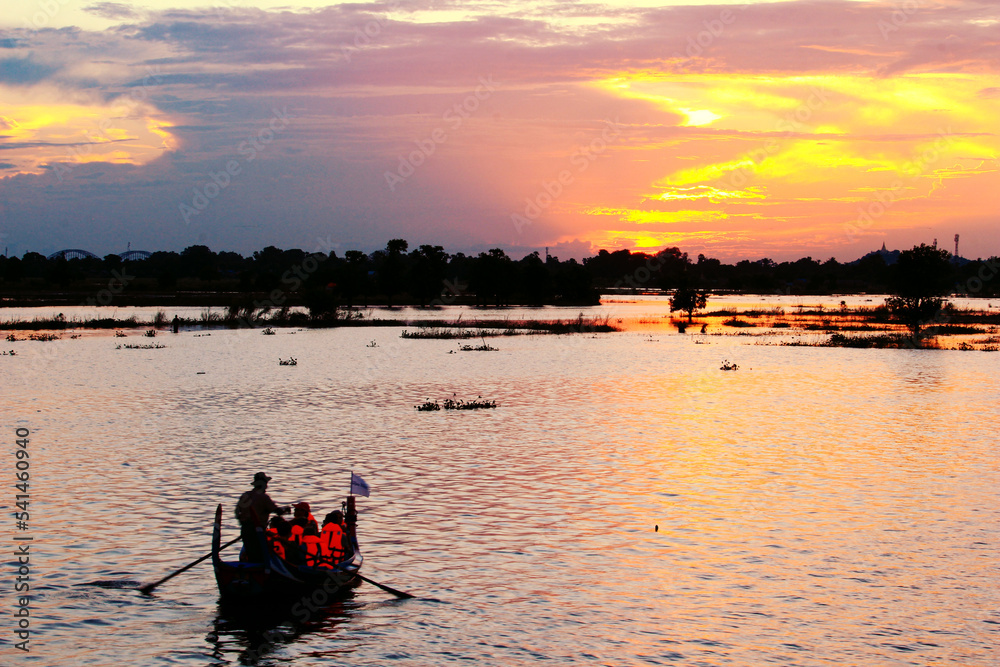 Tourists wearing life jackets sit on small wooden boats to watch the sunset.