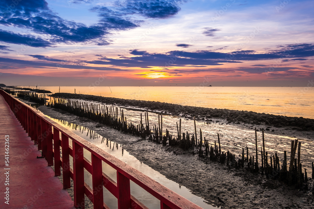 Fototapeta premium A long red wooden bridge, Wooden bridge of nature trail to see the sea, Beautiful sunset, This viewpoint of the sea at Samut Sakhon. Thailand