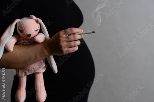 Obraz na plátně a pregnant woman in a black dress and a soft toy in her hands smokes cigarettes