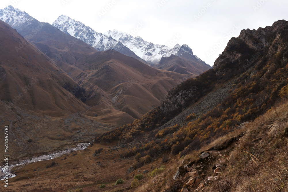 Snow-covered mountains of the Great Caucasus. Hiking in the wild. A mountain river flows in the valley. Autumn landscape. Warm tones. Kabardino-Balkaria. The Rocky Ridge Route