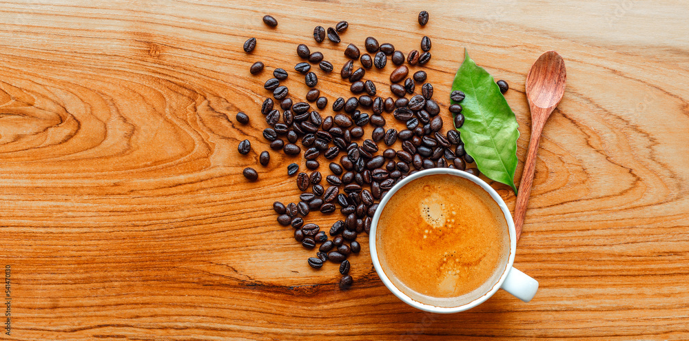 Top view of Espresso coffee cup and dark roasted coffee beans with green coffee leaf  on wooden background