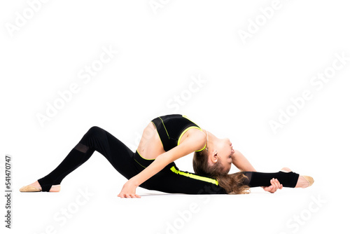 Gymnastic exercises. A flexible little girl in a black tracksuit arches her back and reaches for her leg with her hand. Stretch isolated on white background. Sport, active lifestyle concept