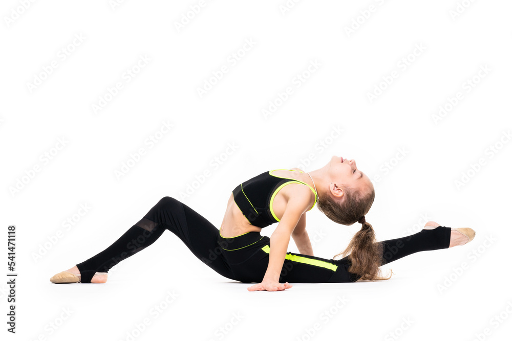Gymnastic exercises. A flexible little girl in a black tracksuit arches her back and reaches for her leg with her hand. Stretch isolated on white background. Sport, active lifestyle concept