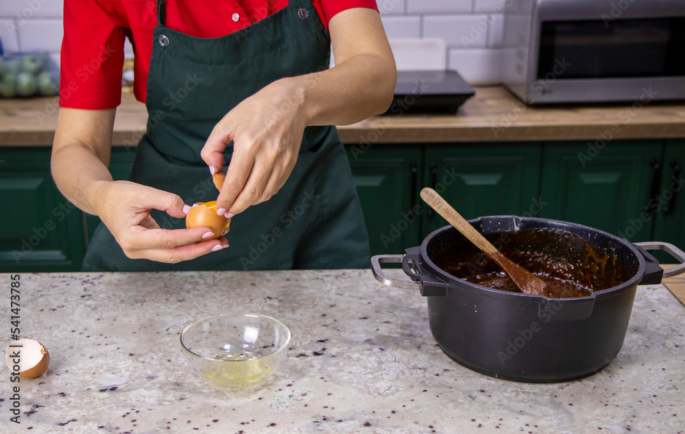 A female pastry chef breaks an egg with her hands to separate the egg white from the yolks before making the dough, eggshells in the background. A female pastry chef breaks an egg with her hands to separate the egg white from the yolks before making the dough, eggshells in the background.