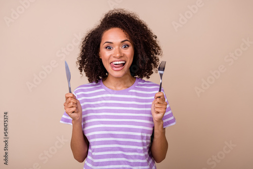 Photo of adorable funky lady wear violet t-shirt showing tongue rising fork knife isolated beige color background