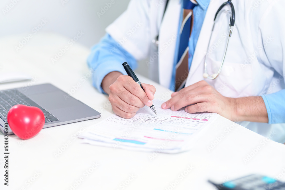 Senior doctor physician using laptop, writing prescription with stethoscope on desk. Old male professional therapist wearing white coat working in hospital. Healthcare, medicine concept. Close up view Senior doctor physician using laptop, writing prescription with stethoscope on desk. Old male professional therapist wearing white coat working in hospital. Healthcare, medicine concept. Close up view