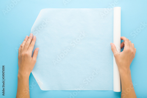 Young adult woman hands holding white roll of baking paper on light blue table background. Pastel color. Closeup. Point of view shot. Top down view. photo
