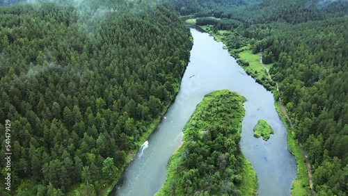 Fog over the endless coniferous forest on a cloudy day. A clean river with a fast current bifurcates and goes around the islands. Cinematic mystical landscape of wild northern nature. Drone footage photo